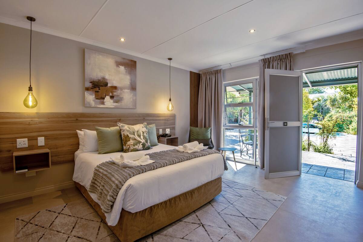 Une chambre d’hôtel moderne avec un grand lit, des tables de chevet, un tableau et une vue sur l’extérieur.