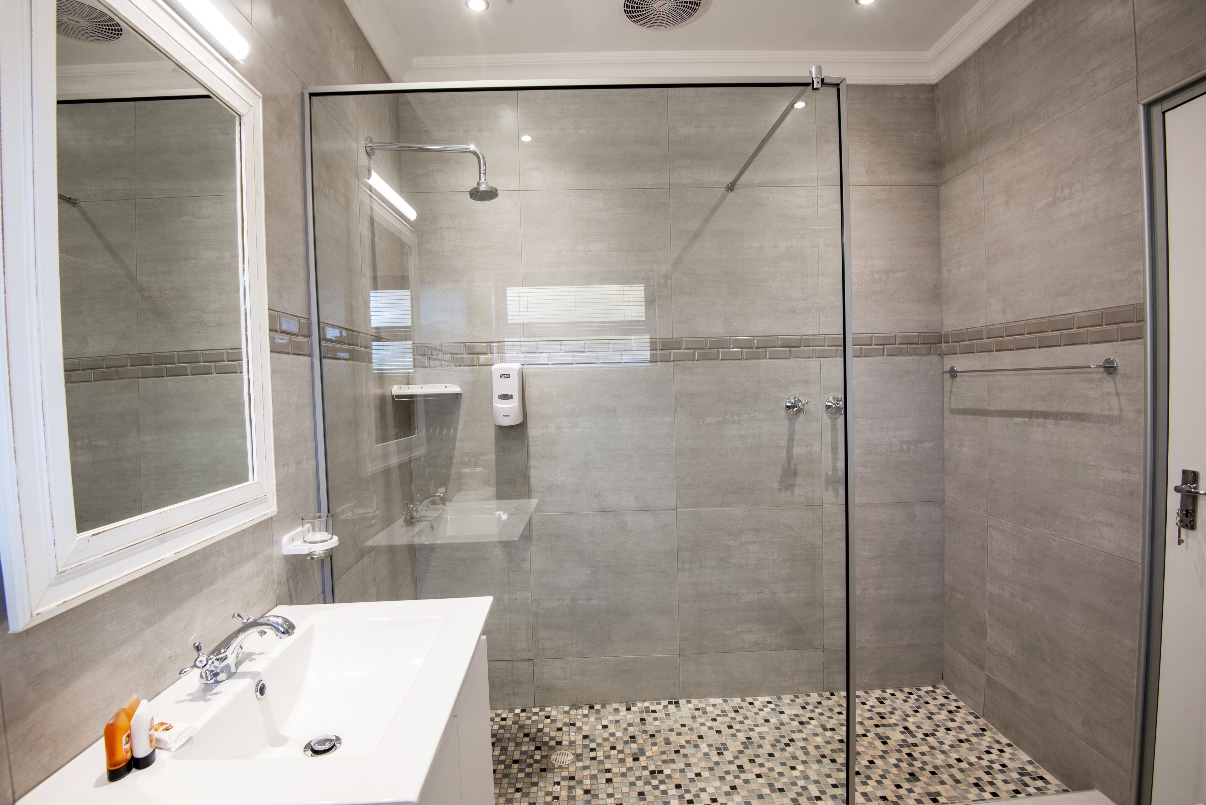 A modern bathroom with a glass-enclosed shower, a white sink, and a tiled floor.