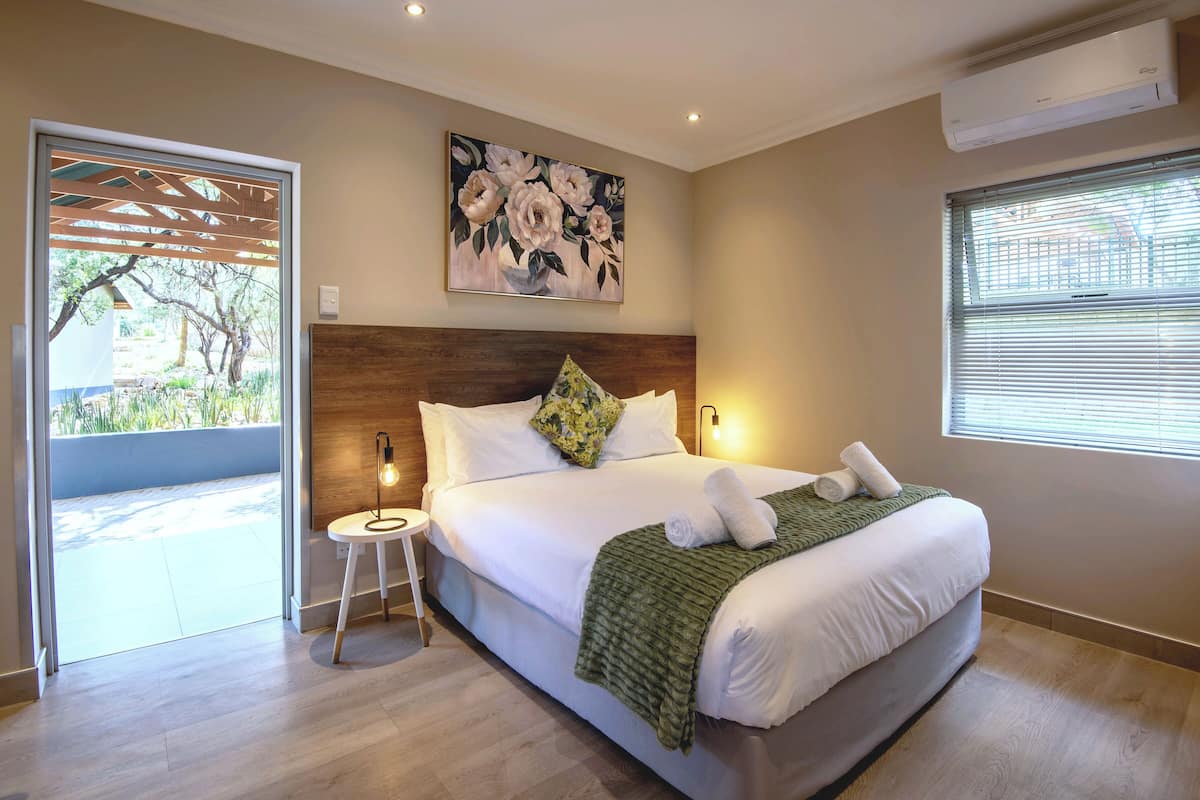 Une chambre à coucher avec un grand lit, une tête de lit en bois, un plaid vert et un tableau accroché au-dessus du lit.