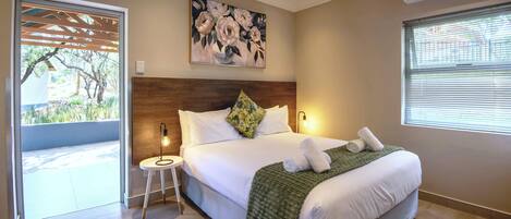 A bedroom with a large bed, a wooden headboard, a green throw blanket, and a painting above the bed.