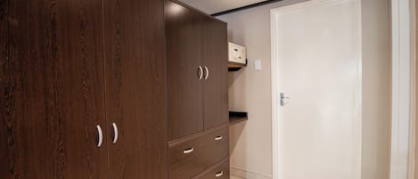 A room with a large wooden wardrobe, a white door, and a small shelf above it.