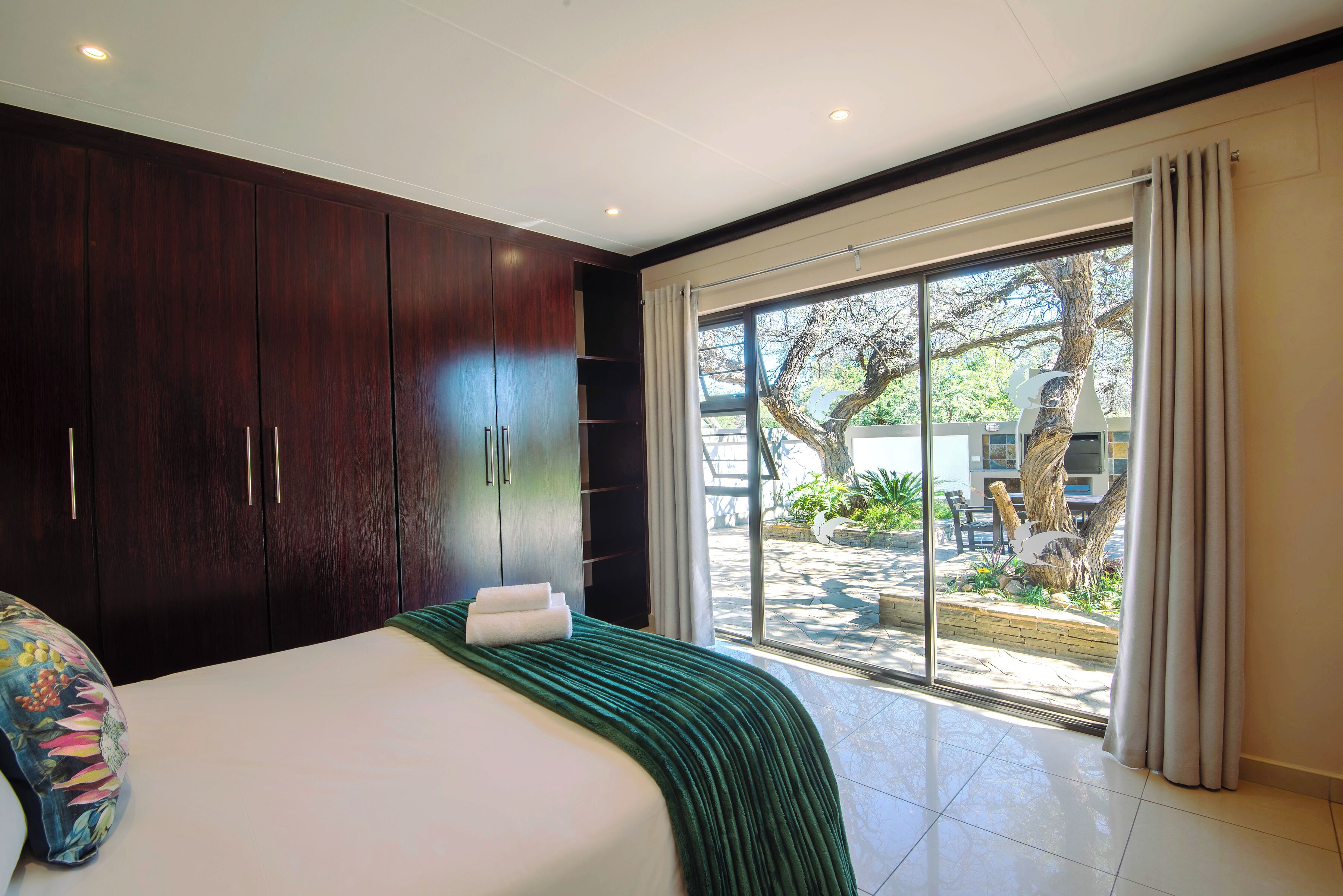 A bedroom with a large bed, dark wooden wardrobe, and a sliding glass door leading to an outdoor area.