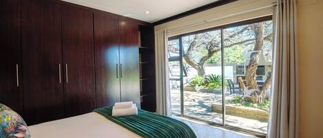 A bedroom with a large bed, dark wooden wardrobe, and a sliding glass door leading to an outdoor area.