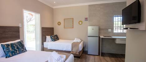 A hotel room with two beds, a desk, a television, and a window.