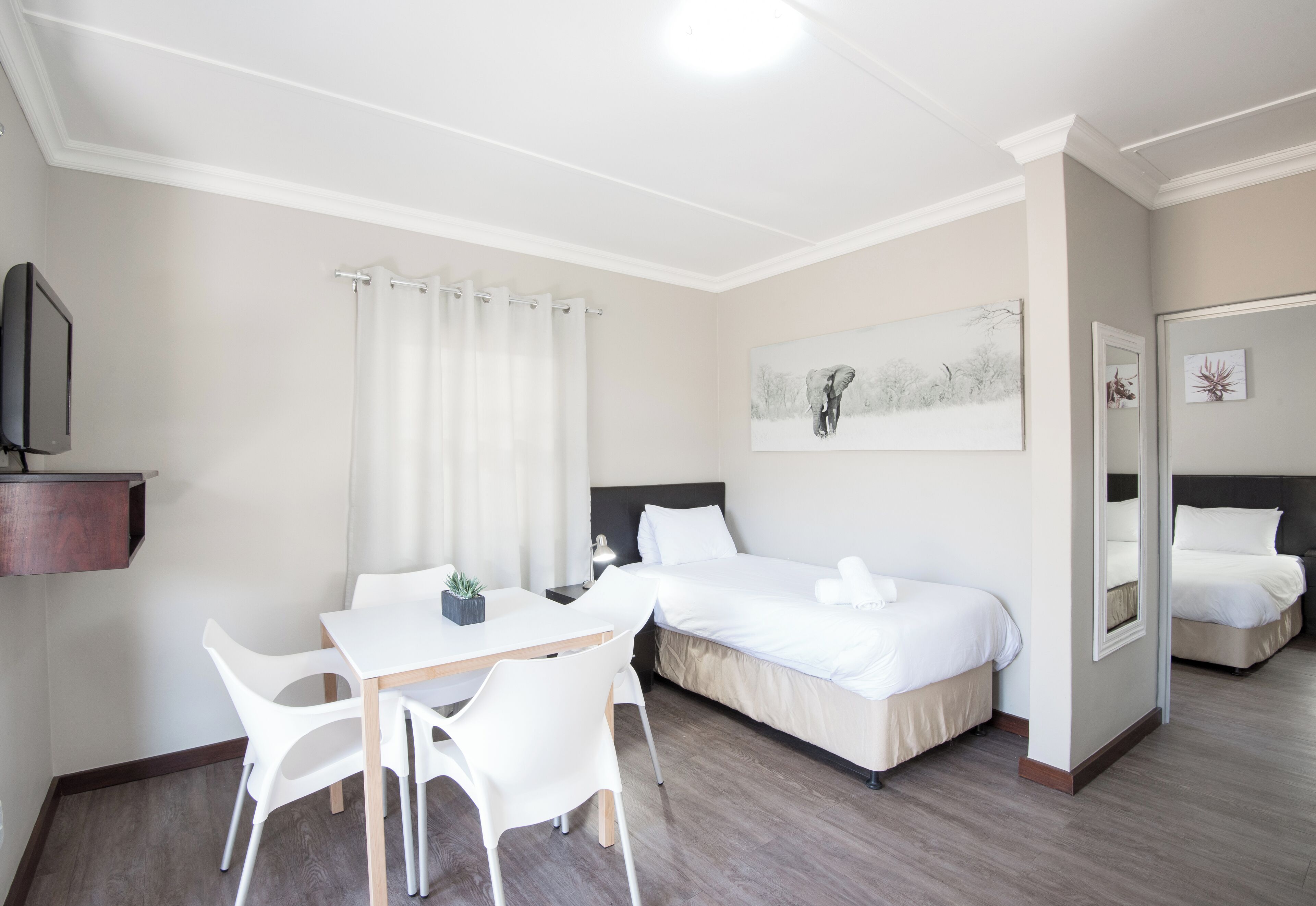 Una habitación de hotel con cama, escritorio con sillas, televisor y un cuadro en la pared.