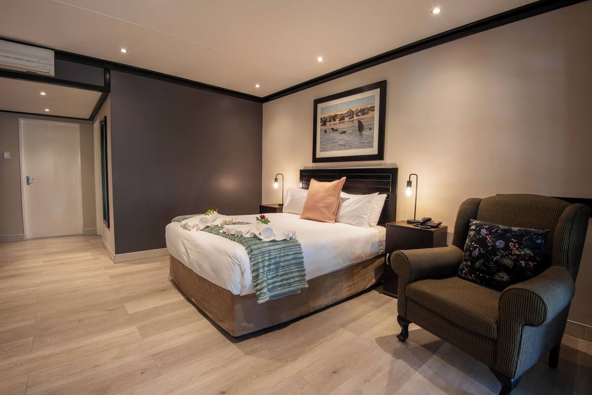 Une chambre à coucher moderne avec un grand lit, une chaise, un tableau encadré au mur et une porte à l’arrière-plan.