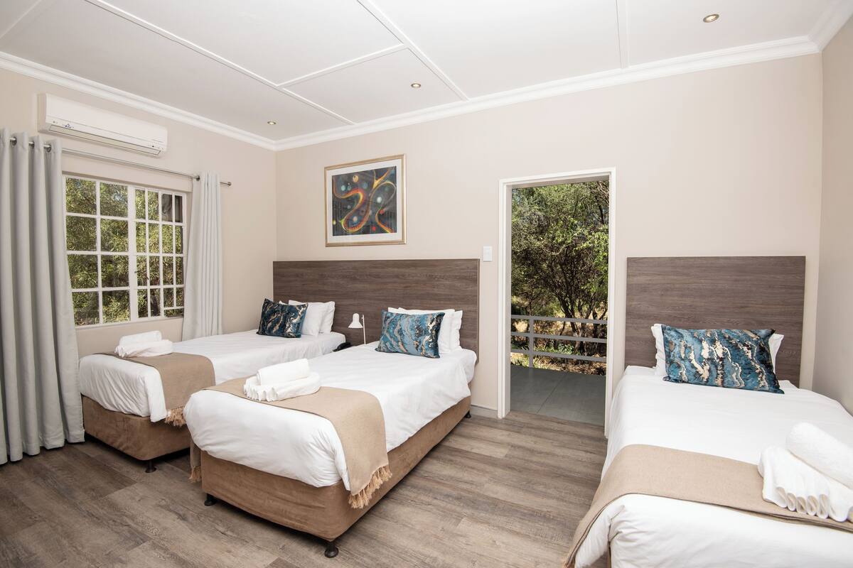 Une chambre d’hôtel avec trois lits, une grande fenêtre et une vue sur la verdure.