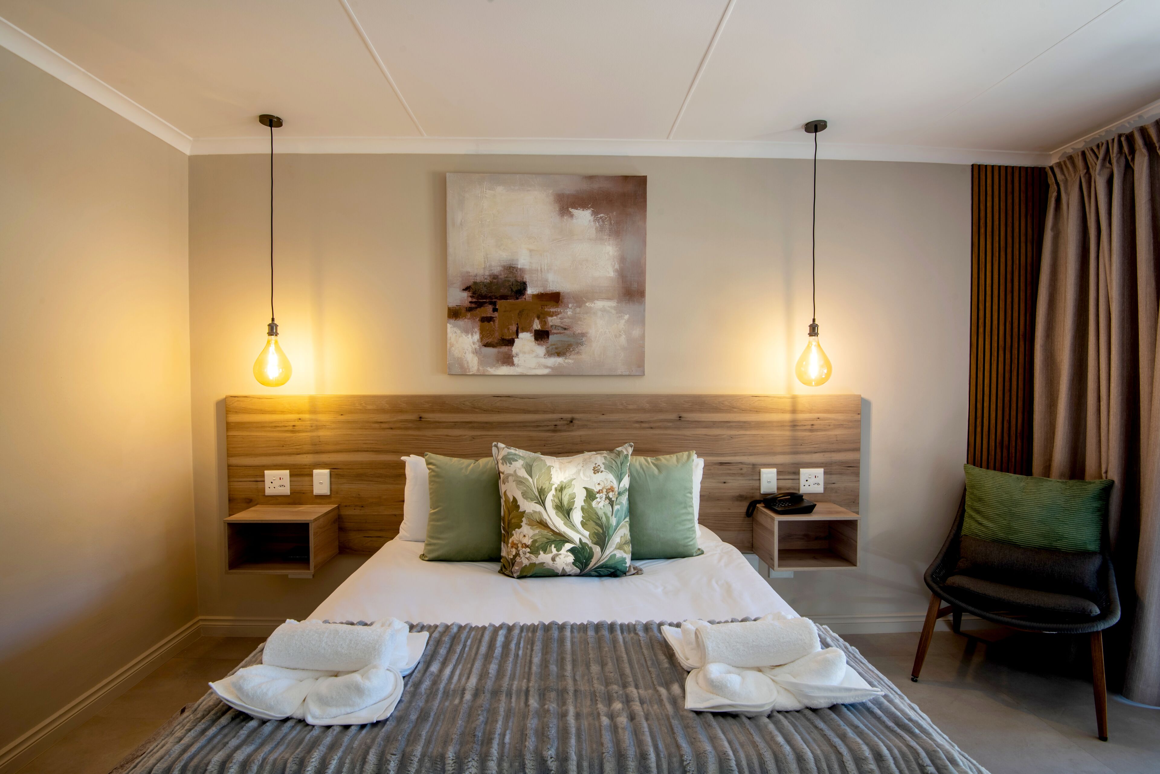 Una camera d'hotel con un letto grande, due comodini, una sedia e un quadro appeso al muro.