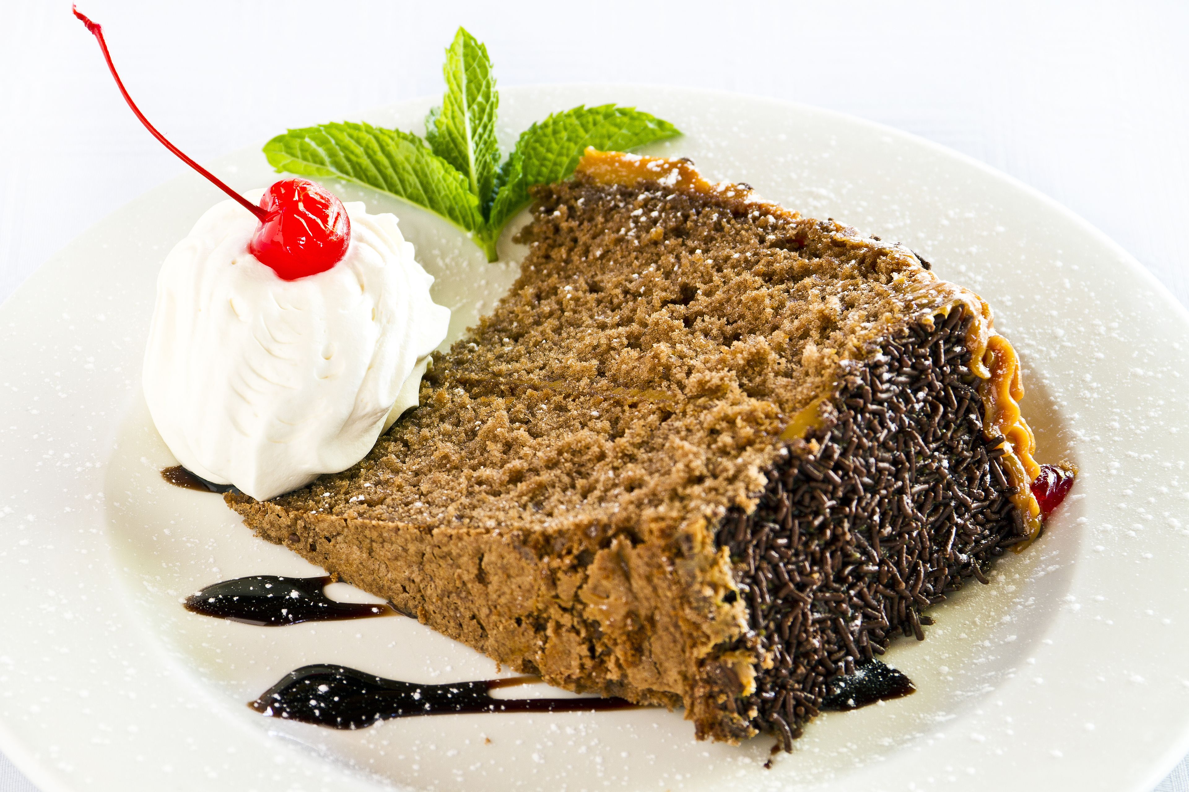Una rebanada de pastel de chocolate con crema batida y una cereza sobre un plato blanco.
