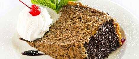 Una rebanada de pastel de chocolate con crema batida y una cereza sobre un plato blanco.