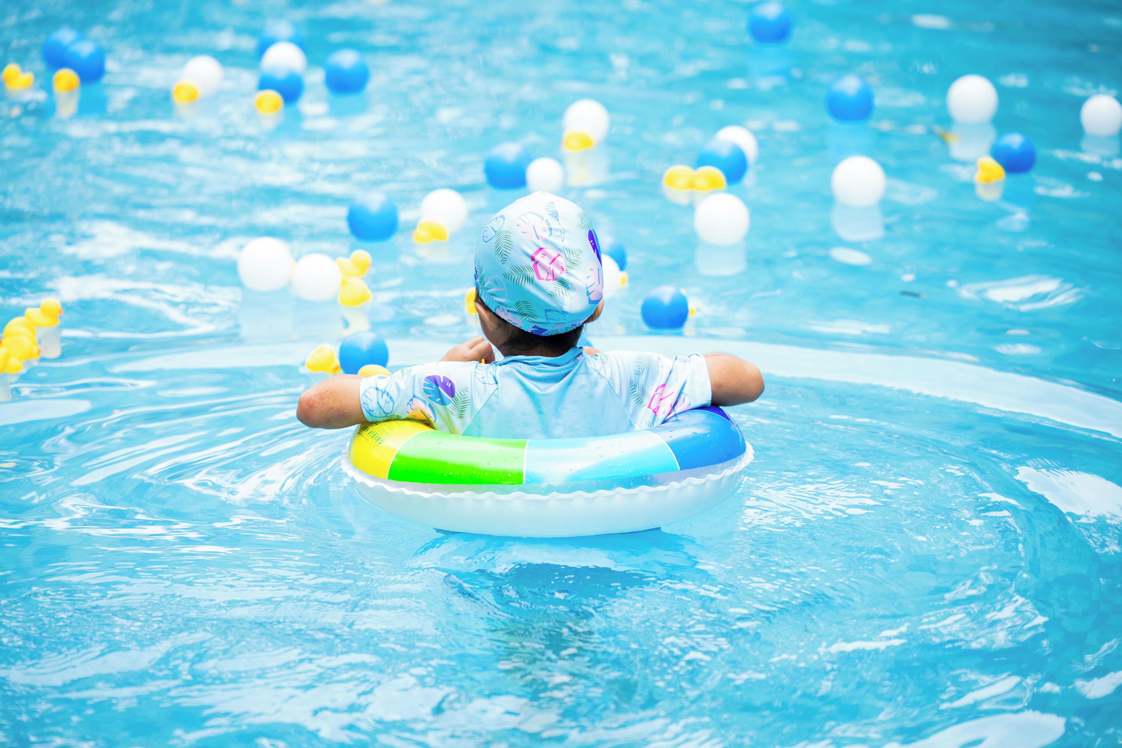 A child floating in a pool with a swim ring, surrounded by floating ducks.