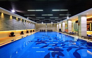Una piscina interior moderna con diseño de mosaico azul, zonas de estar hundidas y un reloj en la pared.