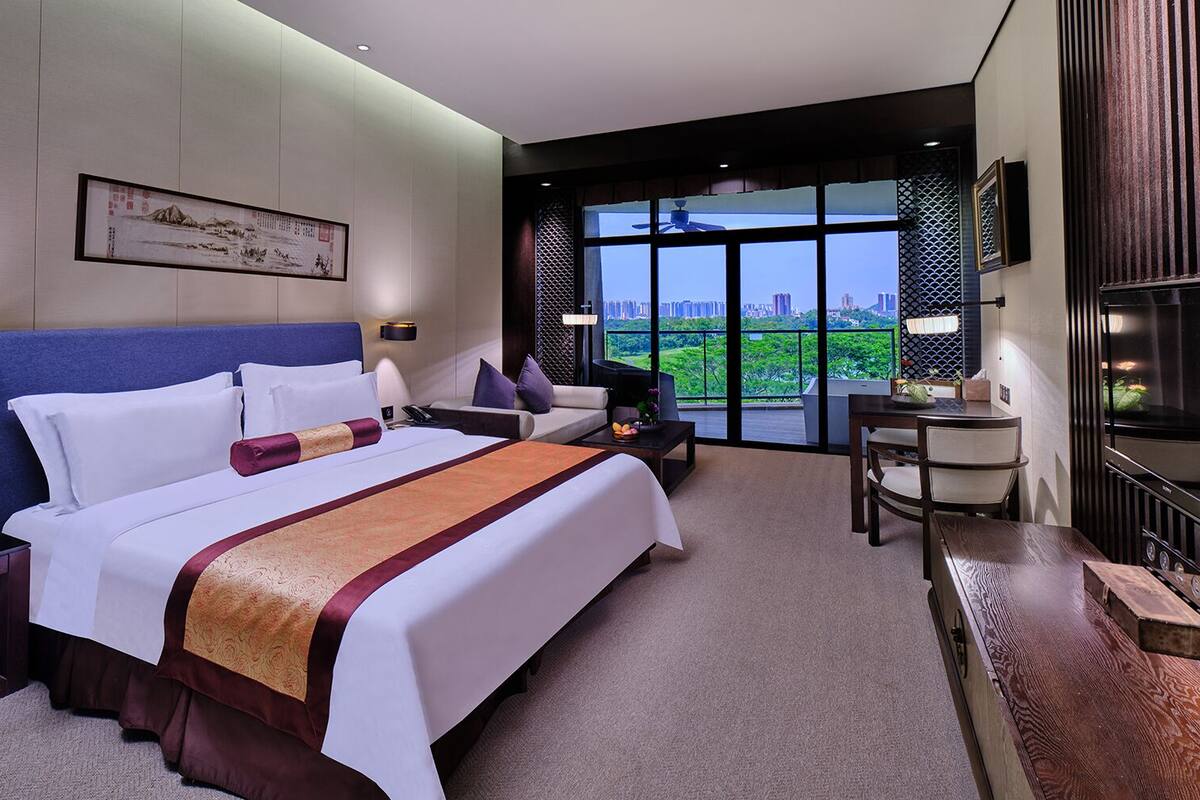 A modern hotel room with a large bed, a desk, a chair, and a TV.