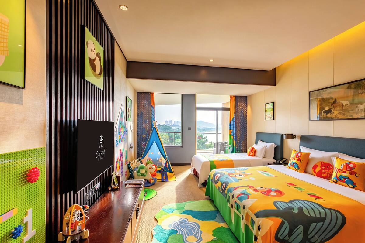 A hotel room with a bed, a desk, a window, and a view of the city.