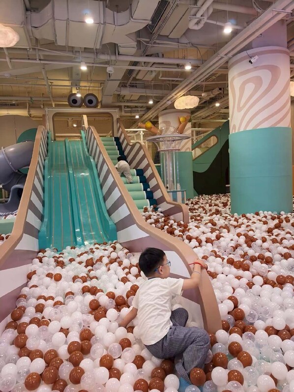 Un área de juegos con toboganes y una piscina de pelotas, llena de pelotas blancas y marrones.