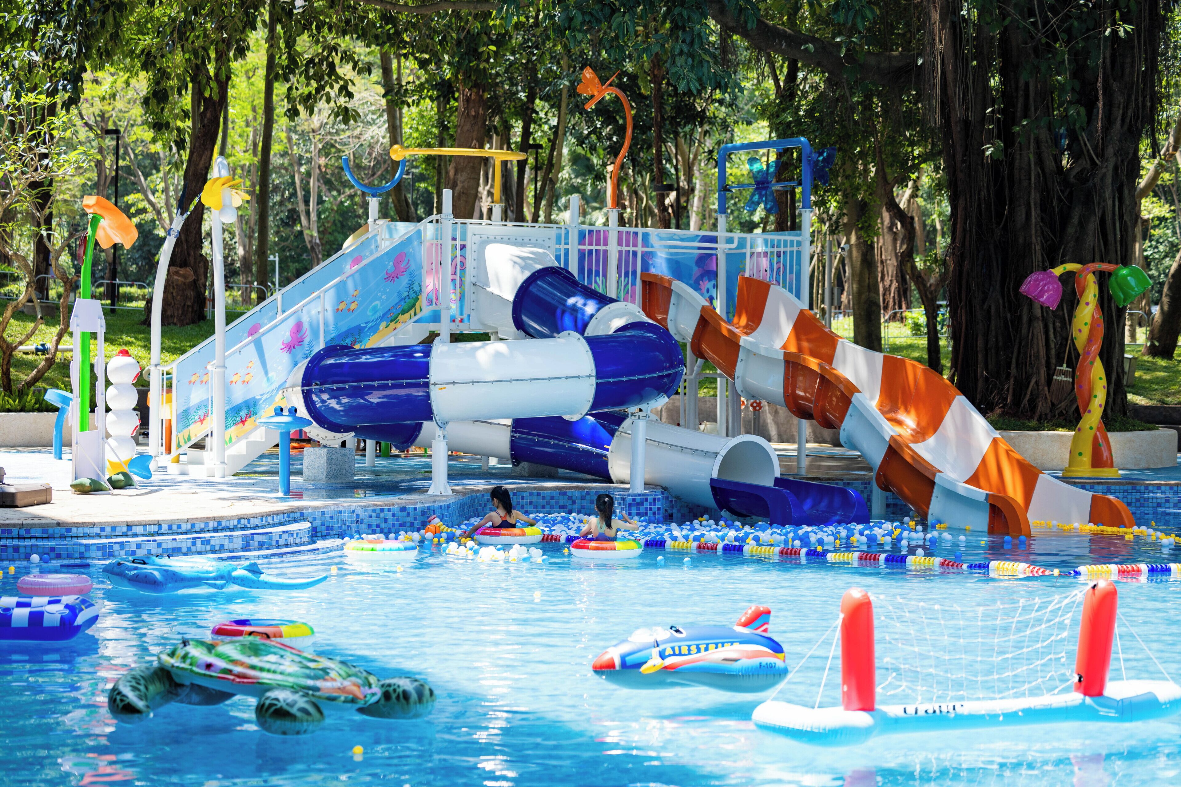 A water park with slides, inflatable rafts, and a pool area surrounded by trees.