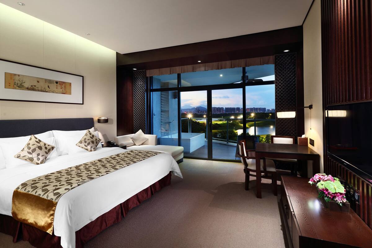 A hotel room with a large bed, a desk, and a view of a cityscape.