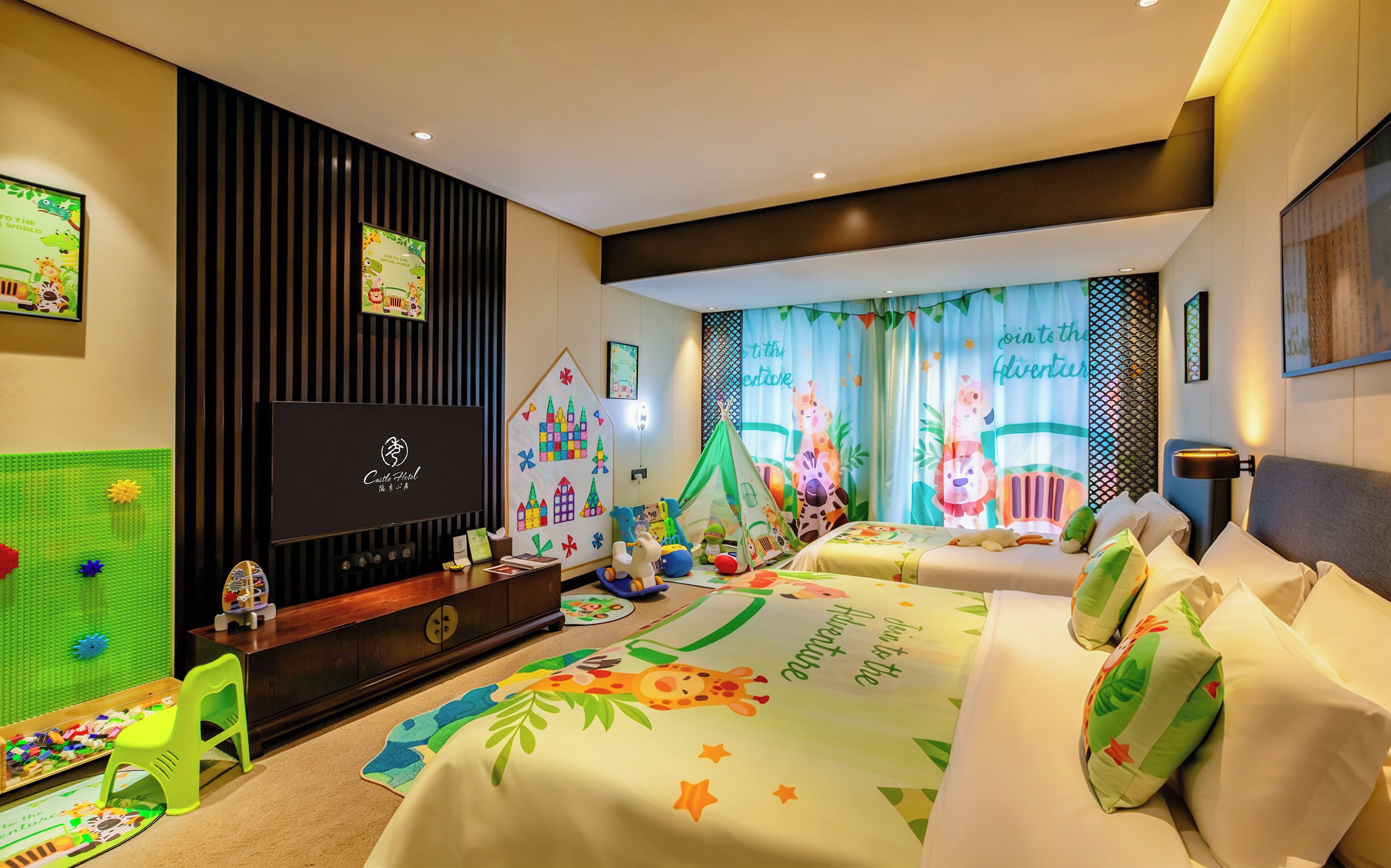 A children's room with a play area, two beds with animal-themed bedding, a television, and a desk with toys.