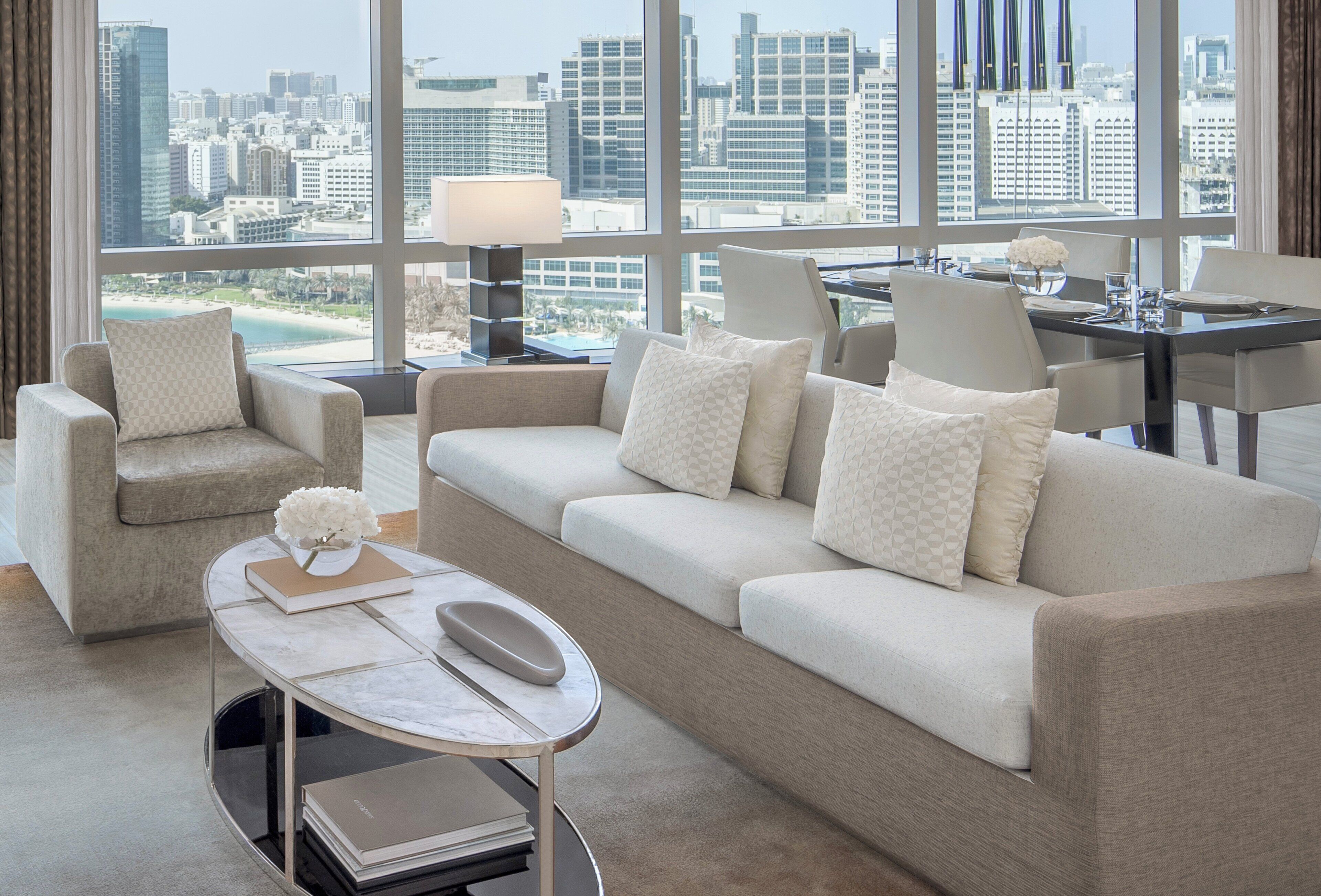 A modern living room with a large window offering a city view, a sofa set, a coffee table, and a dining area.