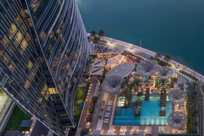 Ovenudblik over et moderne hotel med swimmingpool, udendørs siddepladser og udsigt til havet.