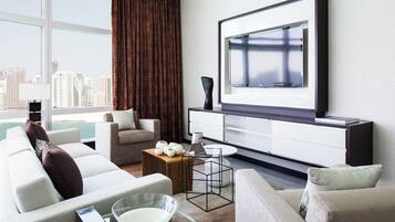 A modern living room with a large TV, comfortable seating, a coffee table, and a view of the city.