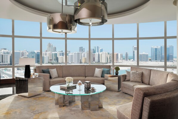 A modern living room with a glass coffee table, a beige sofa, and a city view through large windows.