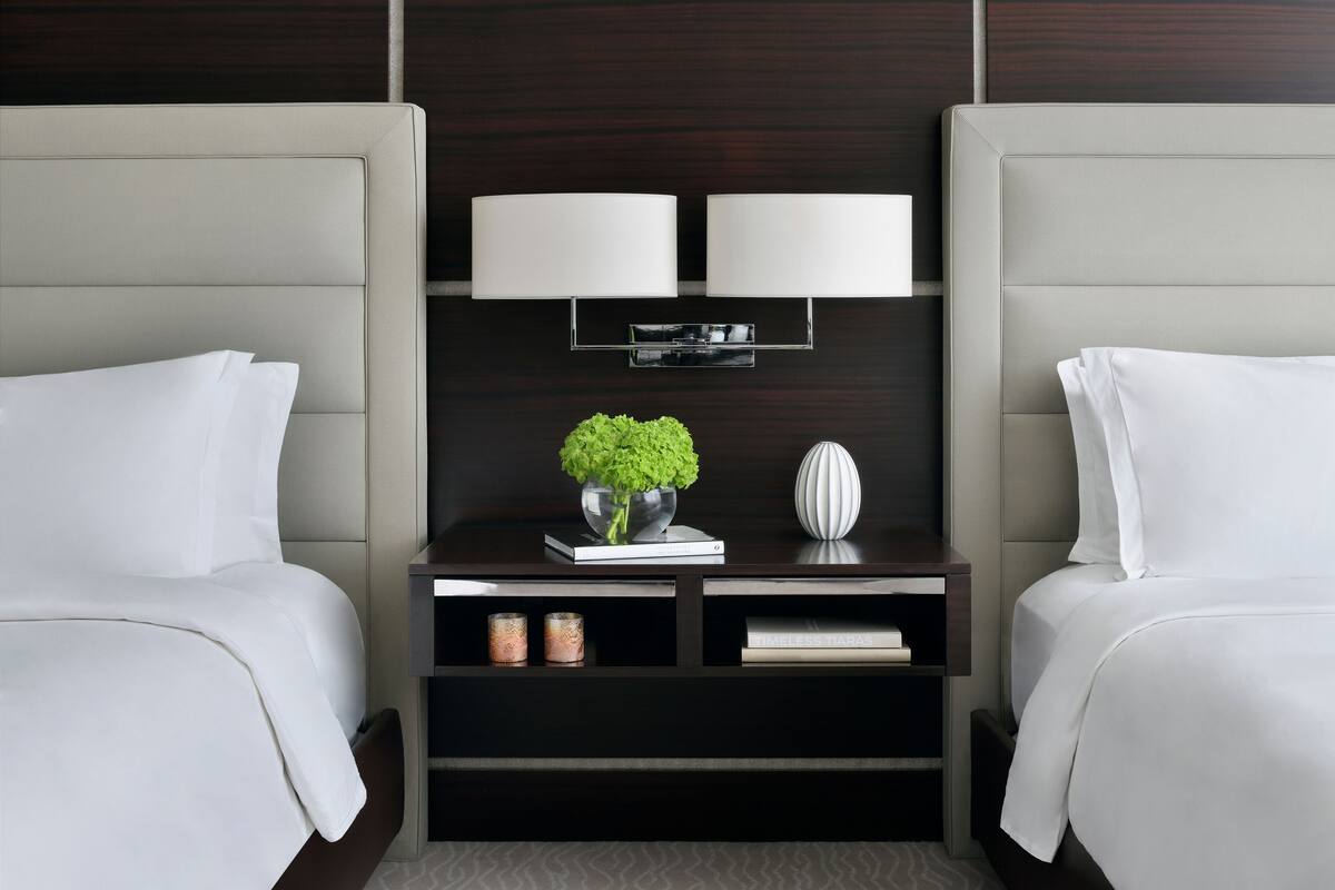 Une chambre d’hôtel avec deux lits, une table de chevet avec une lampe, une petite plante et un vase décoratif.