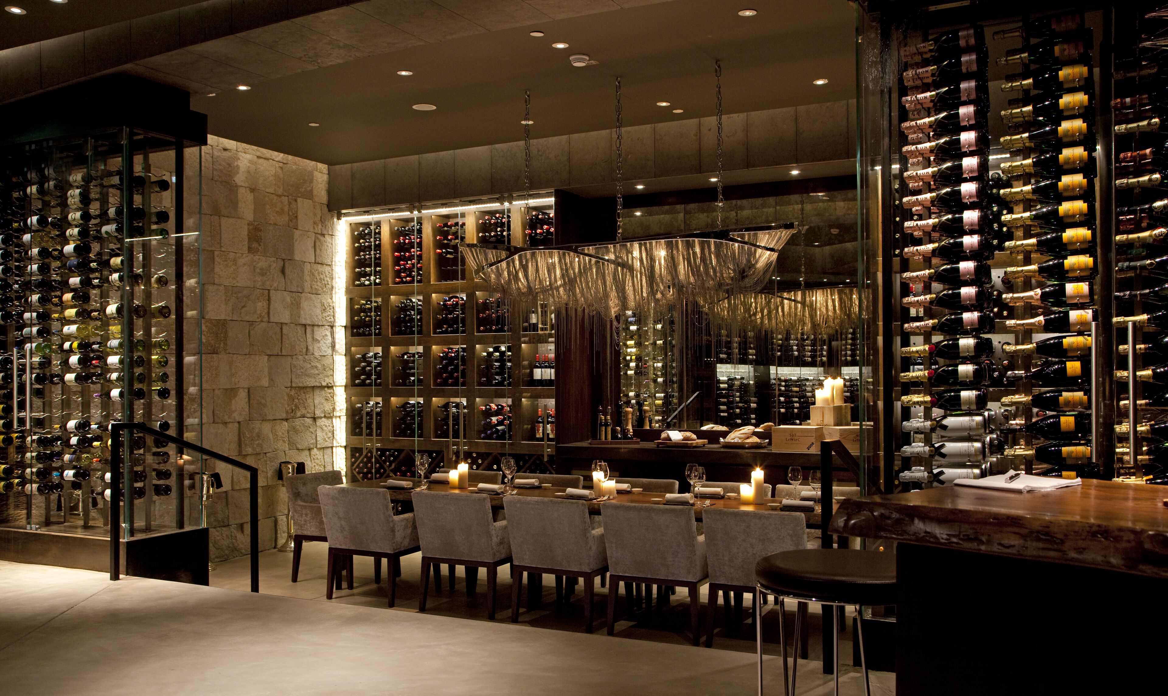A wine cellar with rows of wine bottles, a bar area with stools, and a chandelier.