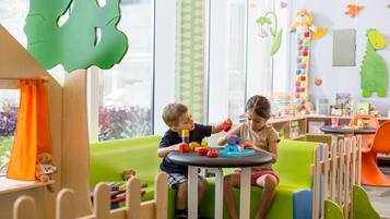 Children can play and learn in this vibrant play area with a cushioned seating area, wooden play structures, and educational wall decals.
