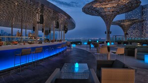 Un bar sur le toit, doté d’un design moderne, comprenant un comptoir, un espace salon et une grande structure en forme de parasol décoratif.