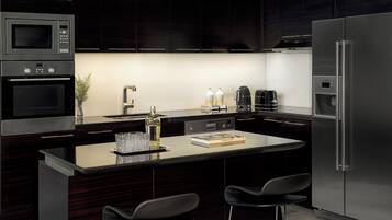 Una cocina moderna con muebles oscuros, un refrigerador de acero inoxidable, un microondas y una cafetera.