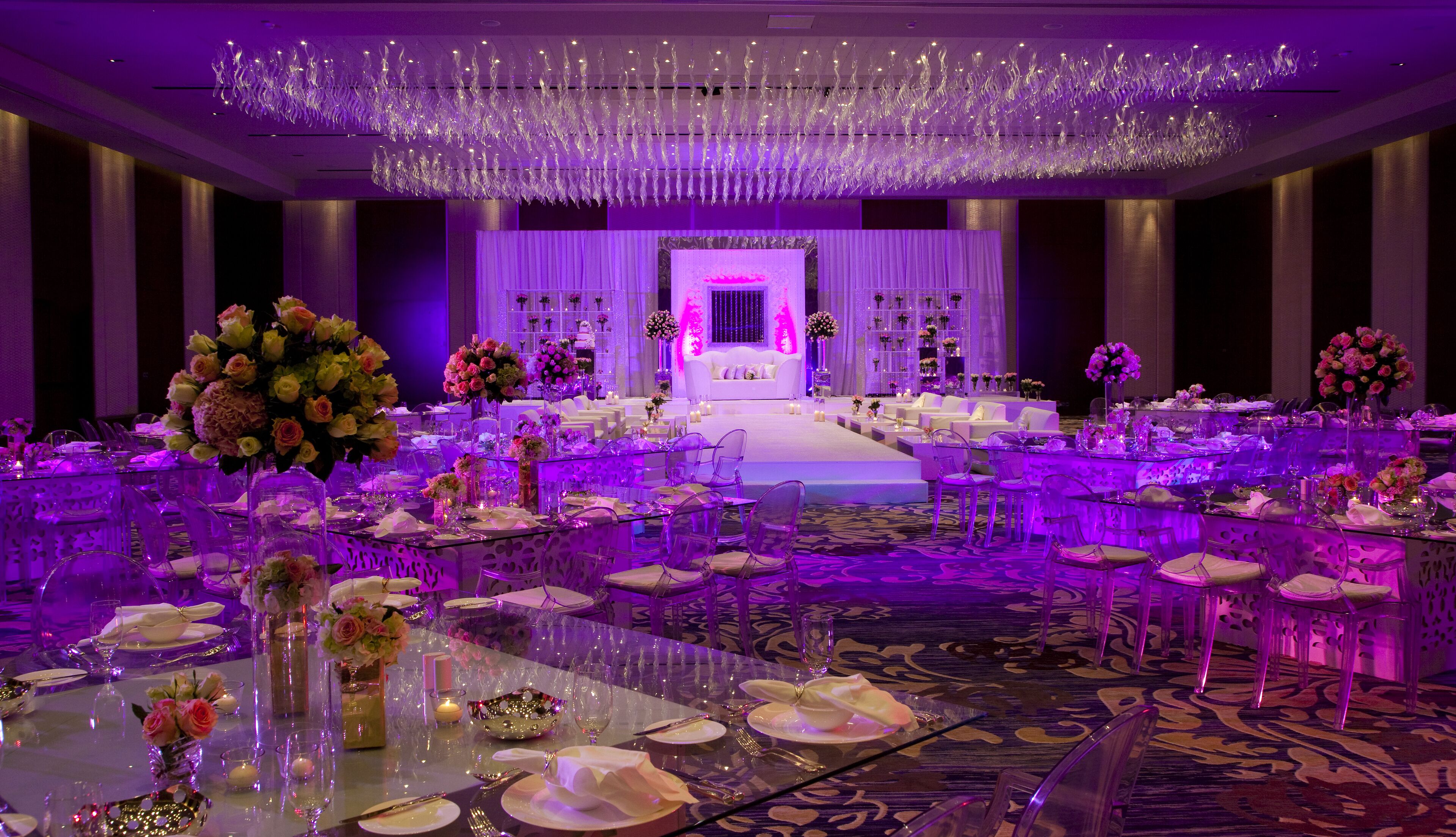 A banquet hall with round tables, chairs, and a stage with a white sofa.