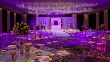 A banquet hall with round tables, chairs, and a stage with a white sofa.