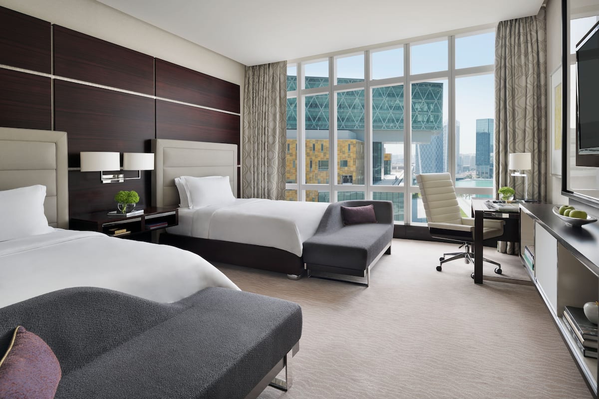 Une chambre d’hôtel avec deux lits, un bureau, une chaise et une grande fenêtre donnant sur la ville.