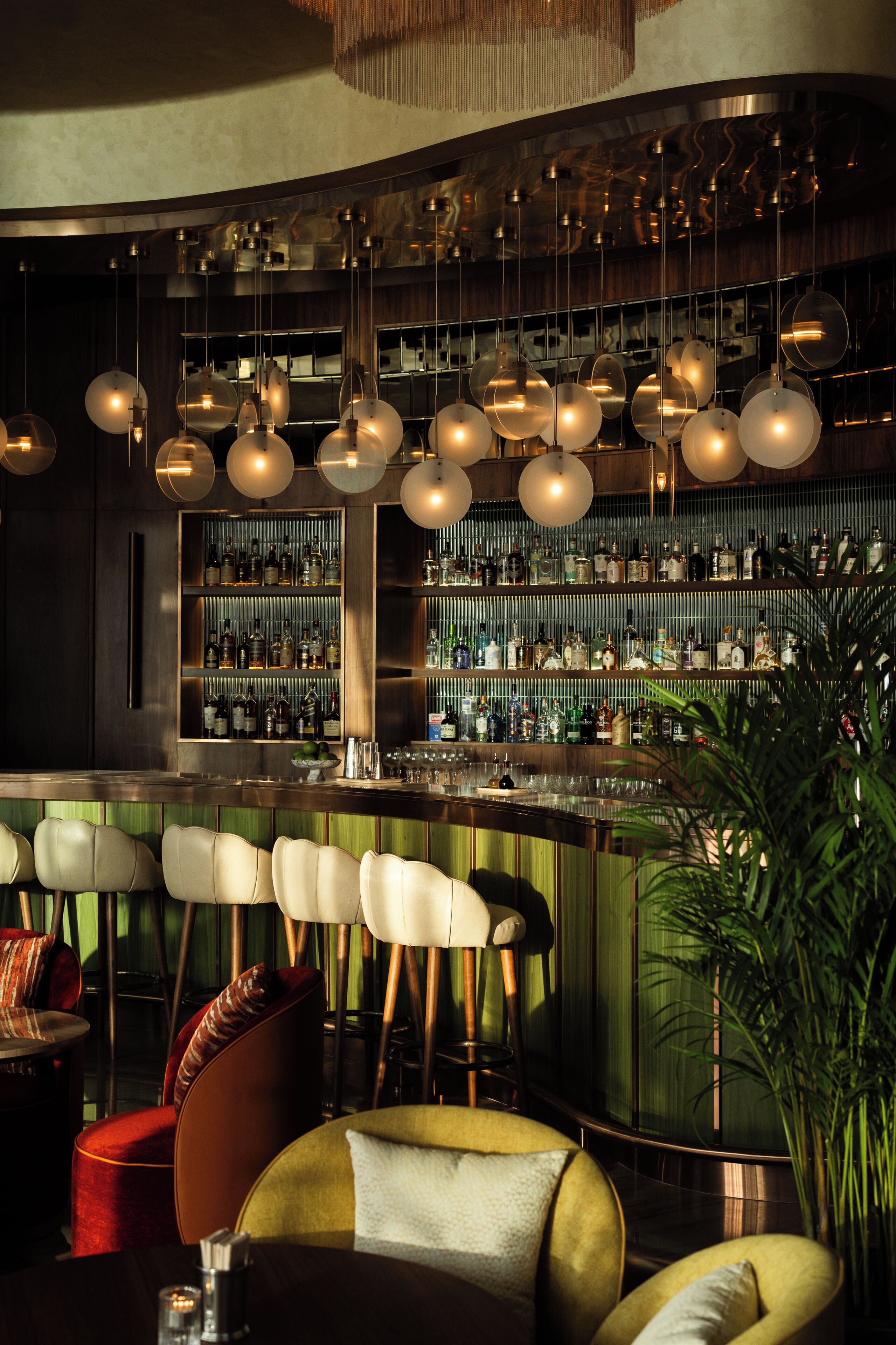 A bar area with multiple hanging light fixtures, bar stools, and shelves stocked with bottles.