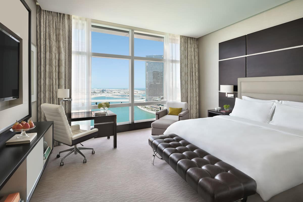 Une chambre d’hôtel avec un grand lit, un bureau, une chaise et une vue sur le paysage urbain et l’eau.
