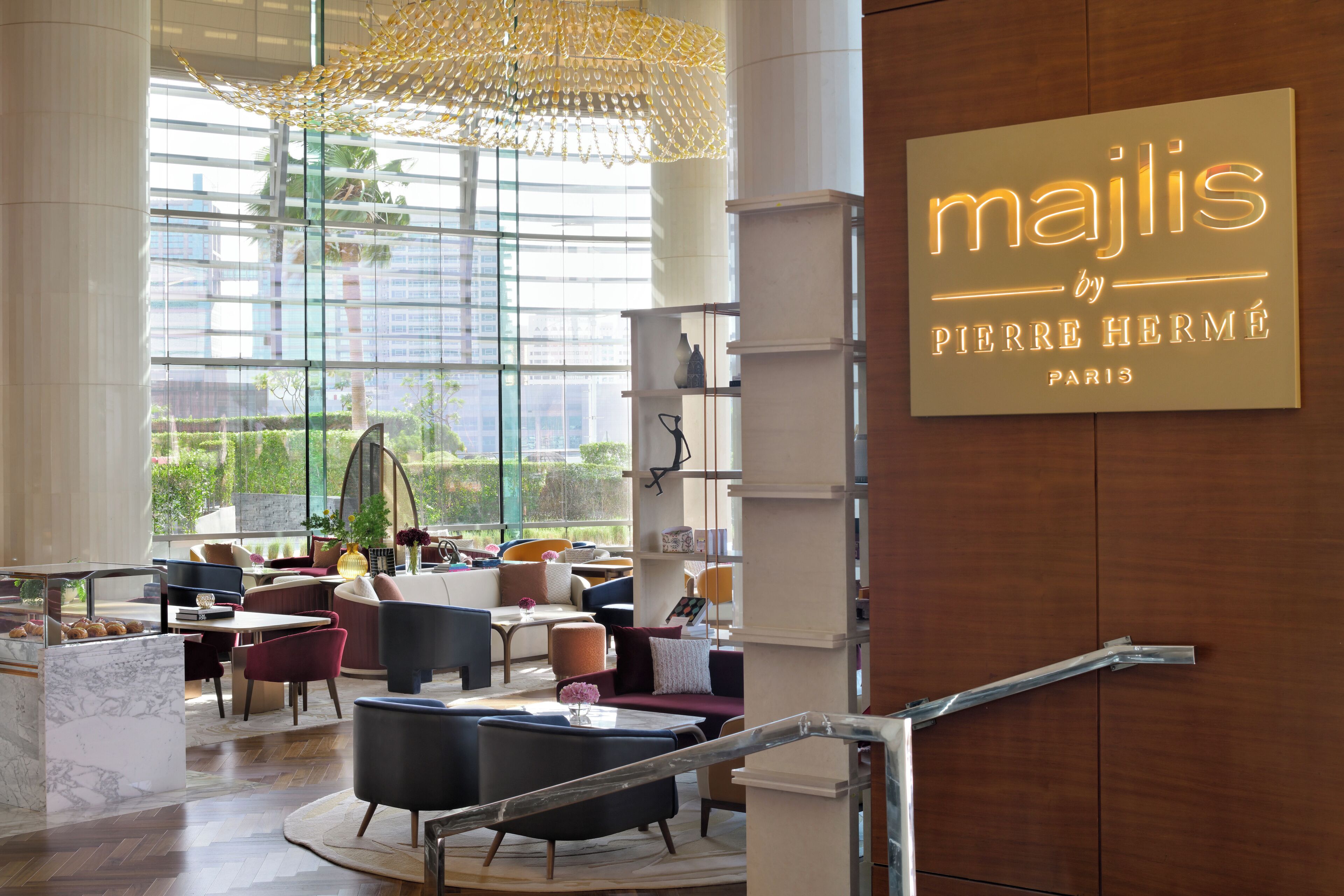 Un moderno vestíbulo de hotel con una gran araña, asientos cómodos y un letrero que dice 'Majlis by Pierre Hermé Paris'.