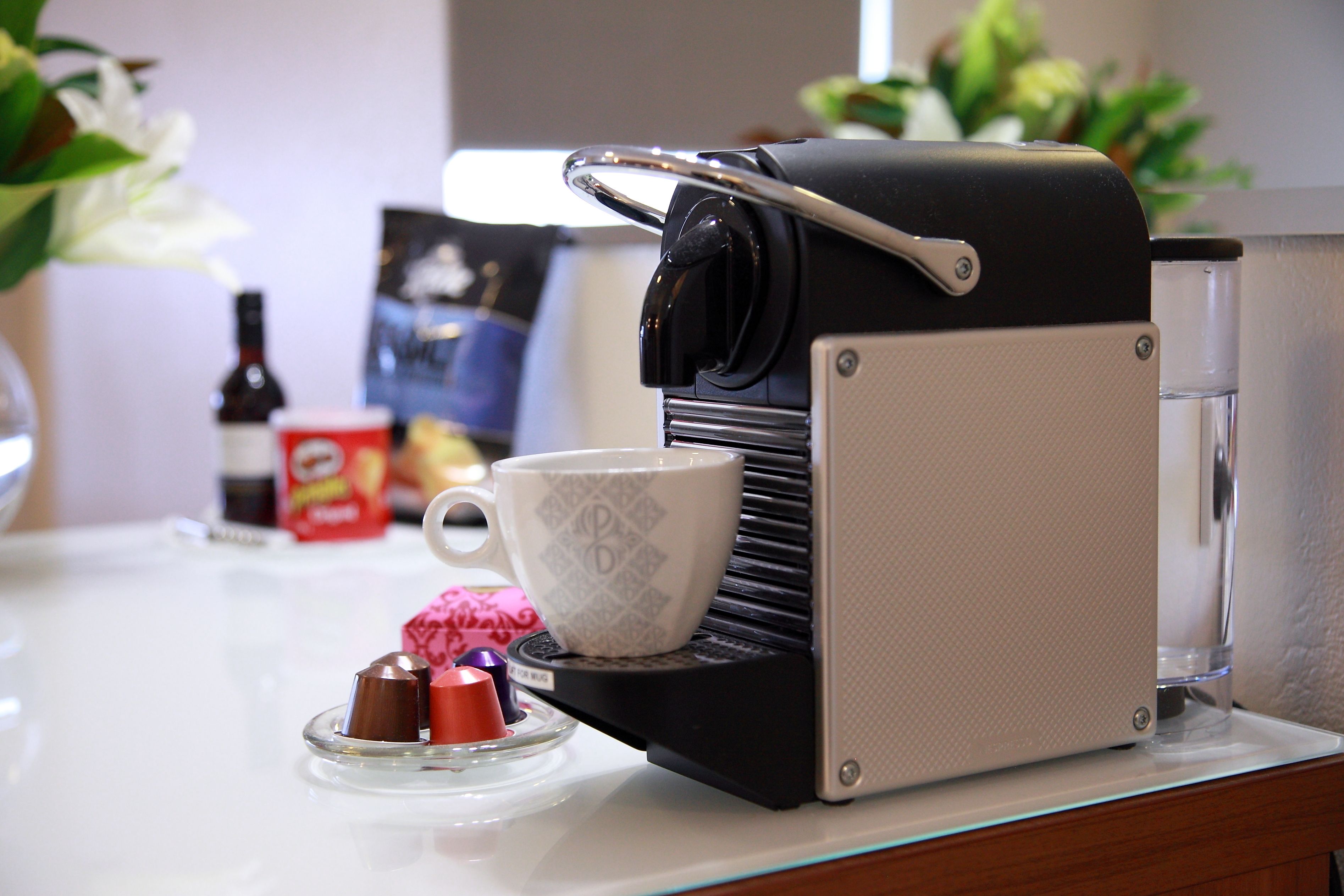 Una cafetera expreso antigua sobre una encimera de cocina, con una taza y dos bombones.