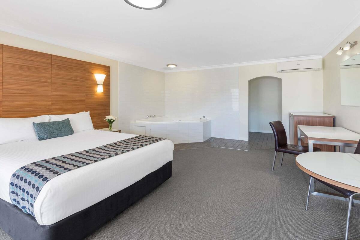 A hotel room with a bed, a desk, a chair, a bathtub, and a shower area.