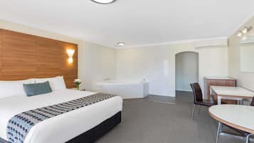A hotel room with a bed, a desk, a chair, a bathtub, and a shower area.