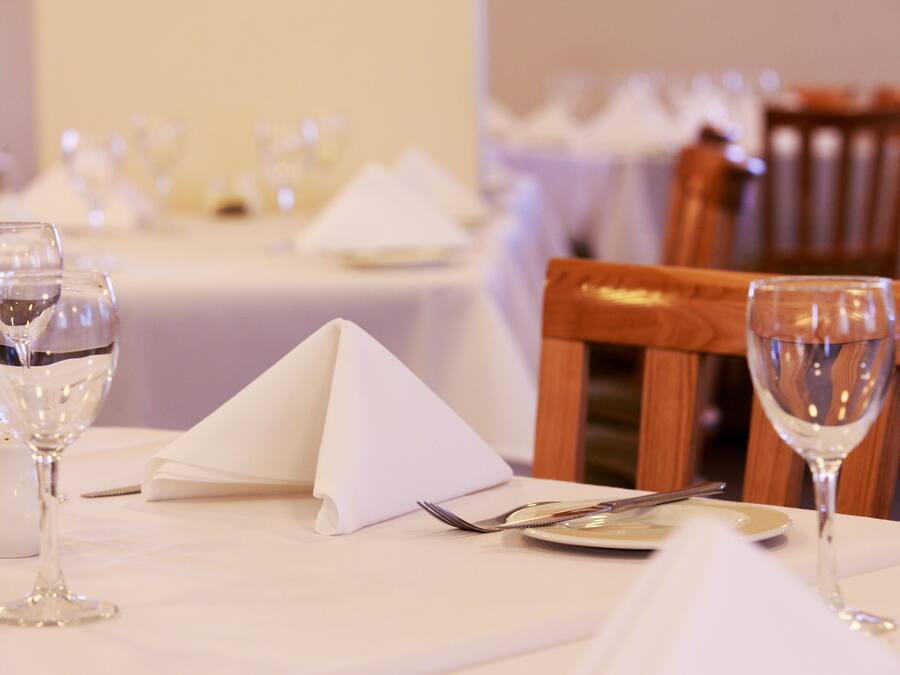 A dining table set with white tablecloths, silverware, and wine glasses.