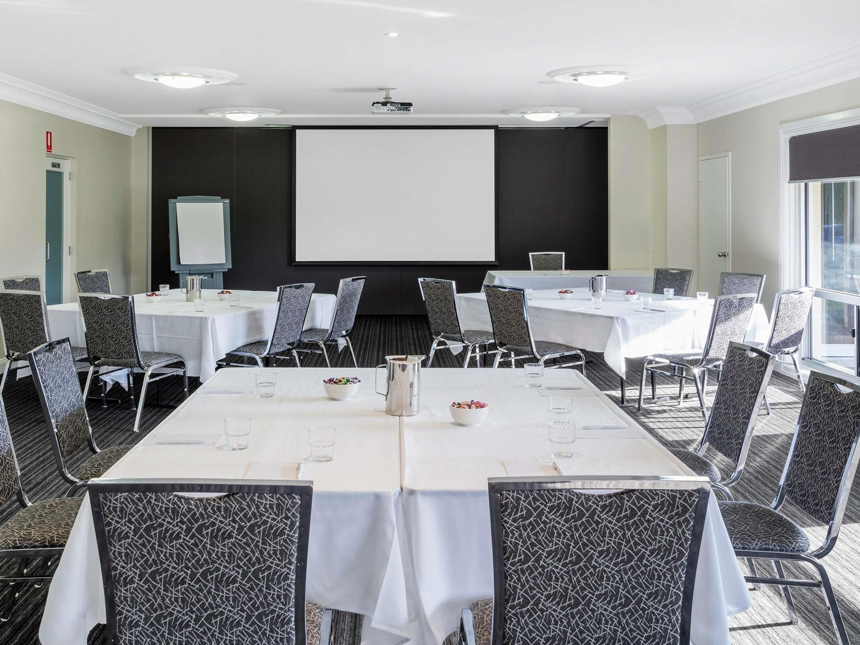 A conference room with tables, chairs, a projector screen, and a large window.