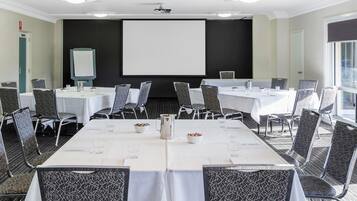 A conference room with tables, chairs, a projector screen, and a large window.