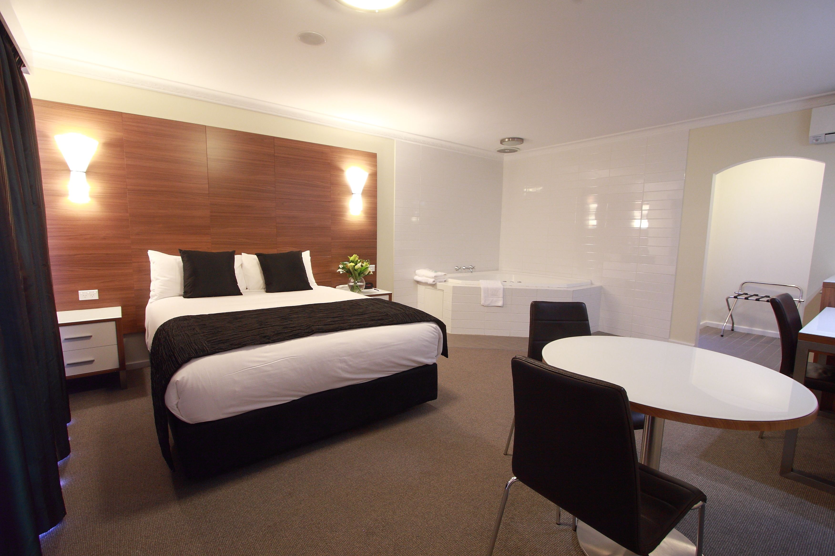Ein Hotelzimmer mit einem großen Bett, einem eigenen Badezimmer mit Badewanne, einem Esstisch und einem Stuhl.