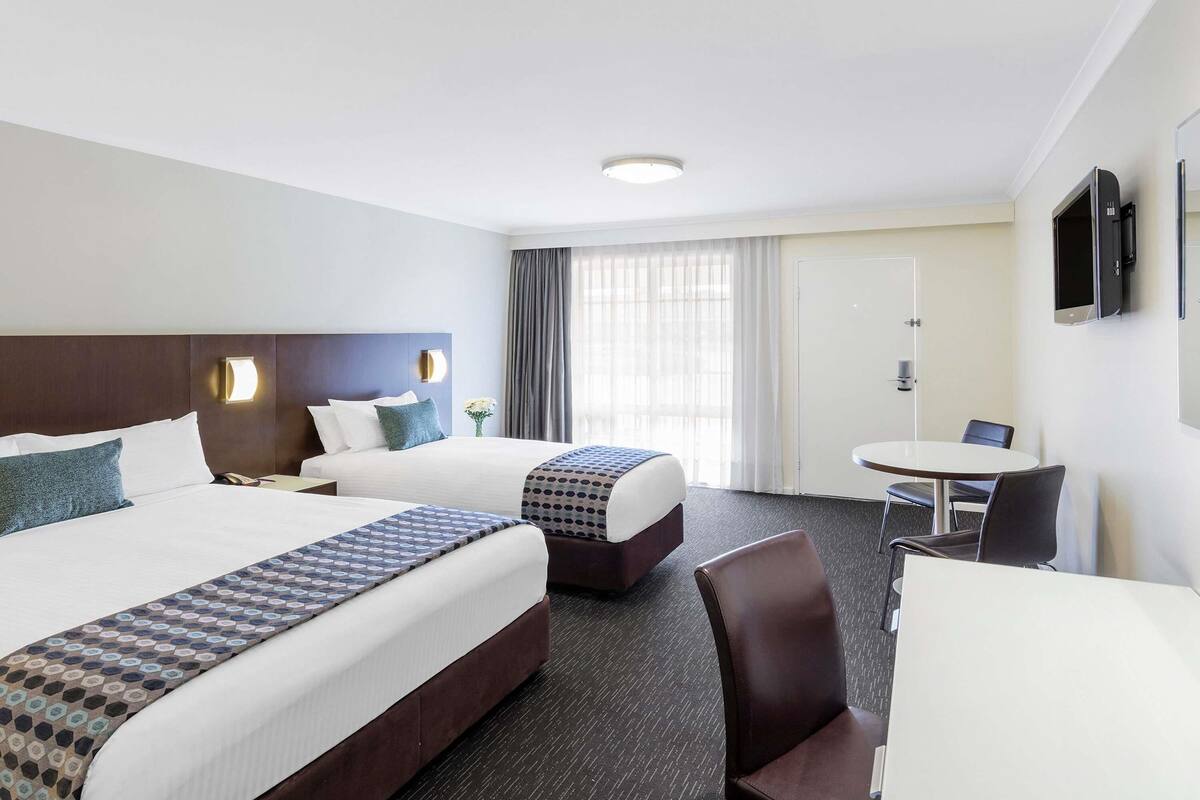 A hotel room with two beds, a desk, and a chair.