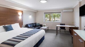 A hotel room with a bed, a desk, a chair, a sofa, a window, and an air conditioning unit. - Mercure Wagga Wagga (Wagga Wagga)