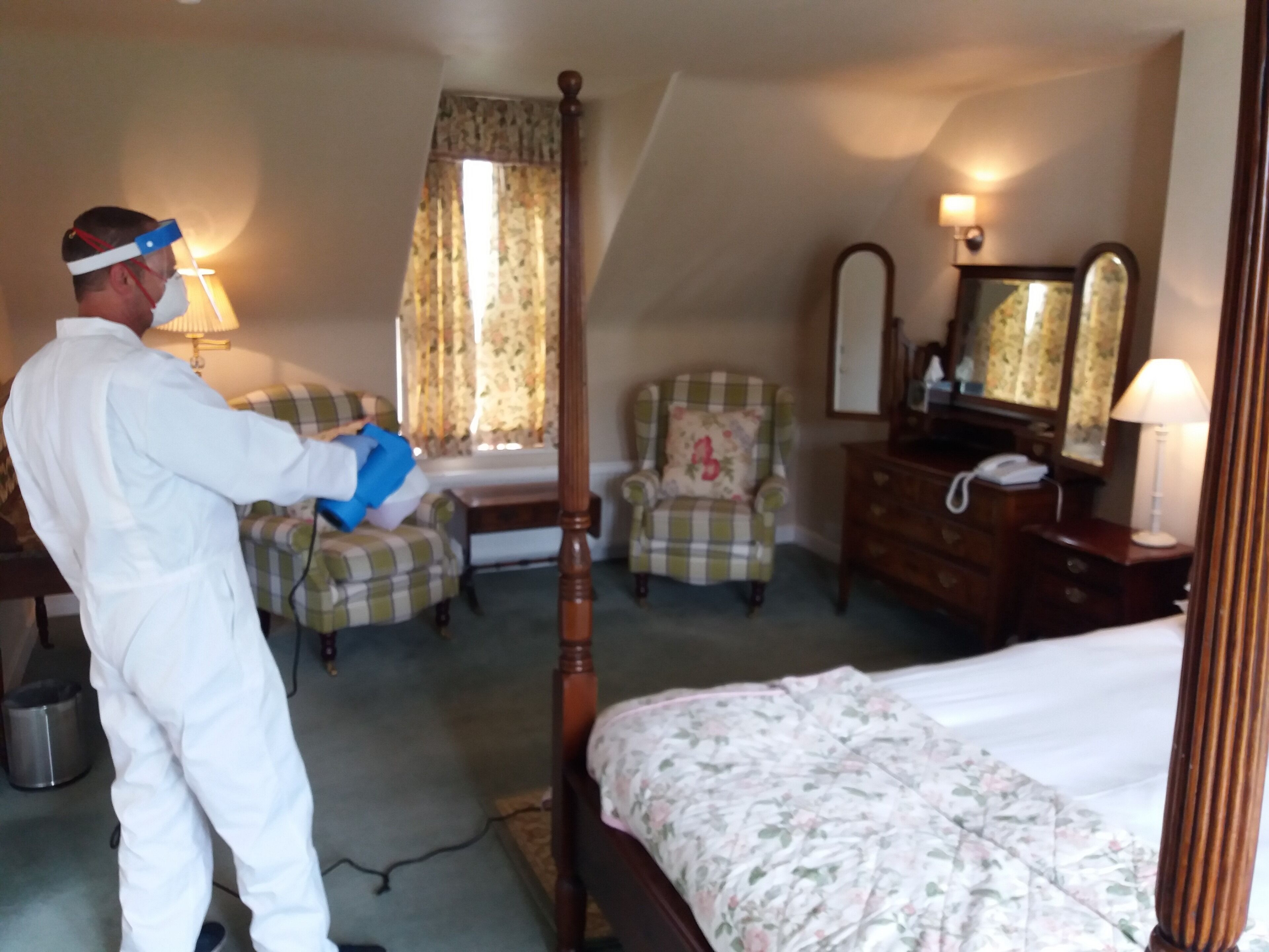 A hotel room with a four-poster bed, a chair, a dresser, and a mirror.