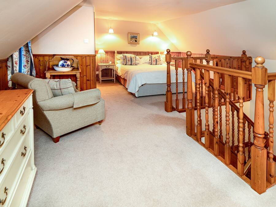 A bedroom with a wooden staircase, a bed, a nightstand, a chair, and a dresser.