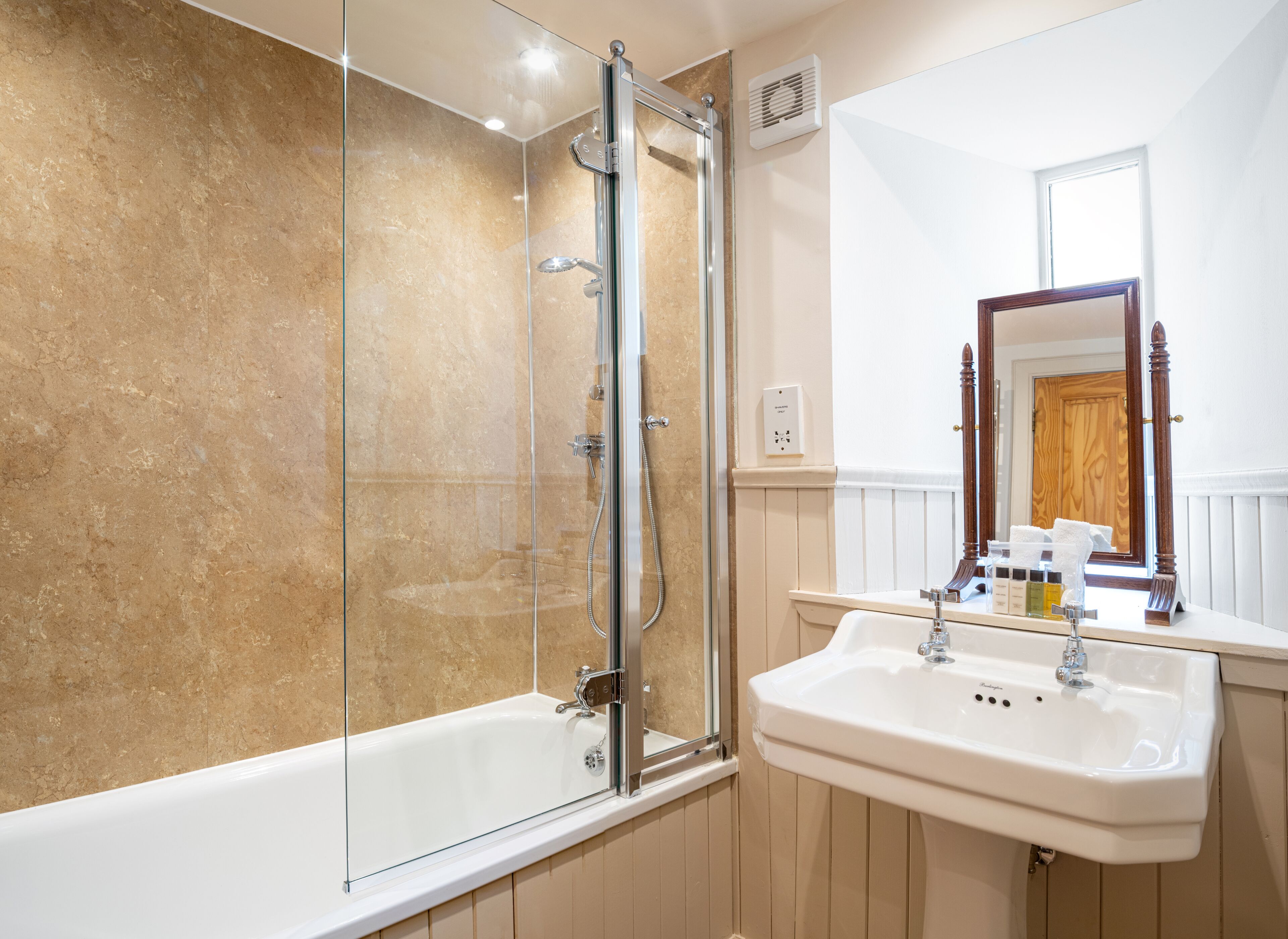 A bathroom with a glass-enclosed shower, a white sink, and a wooden-framed mirror.