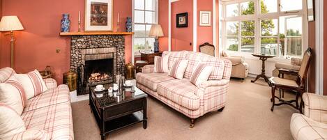 A cozy living room with a fireplace, plaid sofas, and a view through large windows.